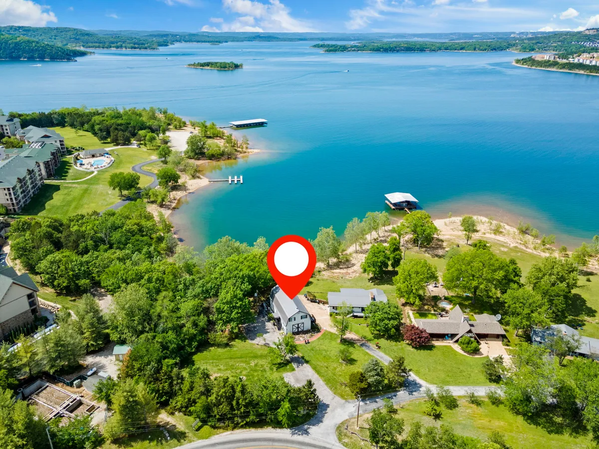 This image captures a beautiful lake view surrounded by lush greenery, with residential structures and a docking area visible. The scene hints at opportunities for boating, fishing, swimming, and picnicking, all set against a tranquil, family-friendly backdrop.