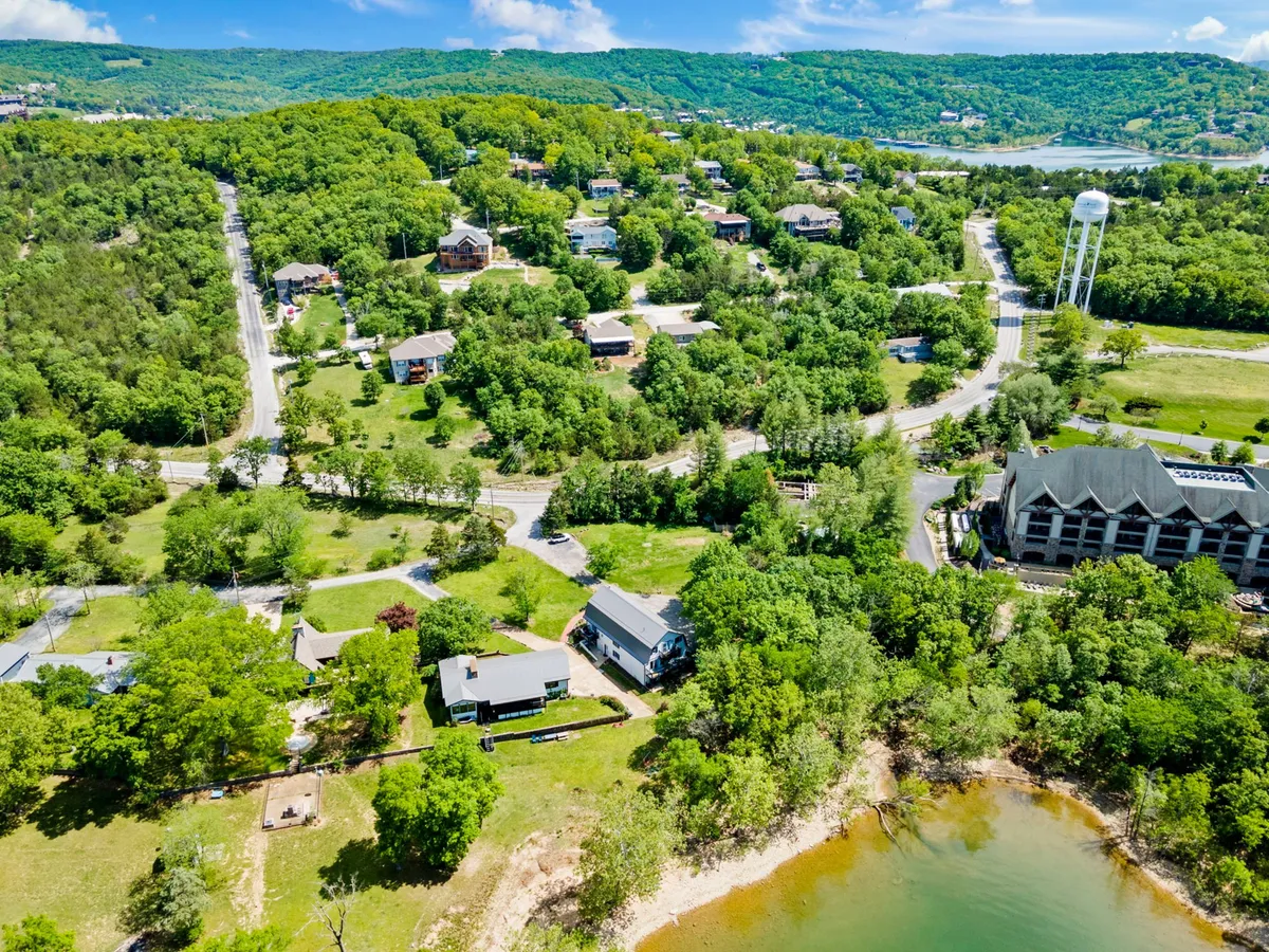 A panoramic view of lush greenery, homes nestled in the Ozark hills, a water tower, and the shoreline of the lake. The landscape is calm and scenic, inviting hiking, boating, and peaceful family gatherings, with sunset hues indicating the close of an active day outdoors.