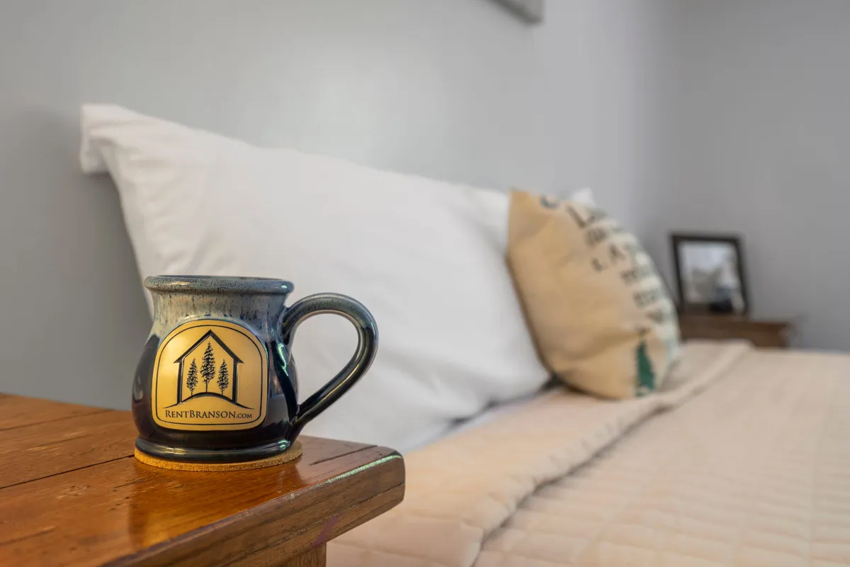 A cozy, inviting sleeping area featuring a well-made bed adorned with plush pillows, a ceramic mug on the nightstand, and a framed photo adding personal warmth. The image conveys a sense of comfort and relaxation, making it an ideal setting for restful nights.