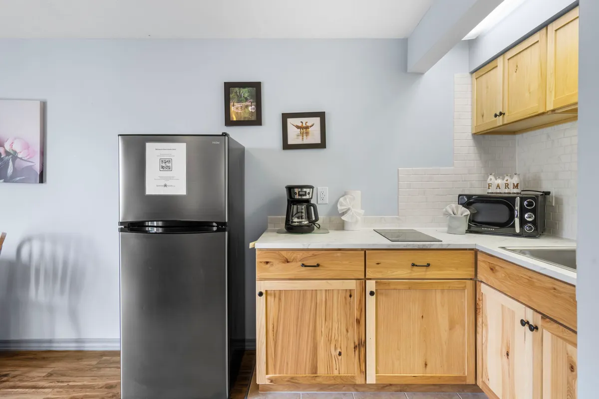 This image features a compact kitchenette with a black refrigerator, wooden cabinets, a microwave, and a coffee maker. The layout is efficient and inviting, ideal for preparing small meals and brewing morning coffee. The lighting and decor add a cozy touch to the setup.