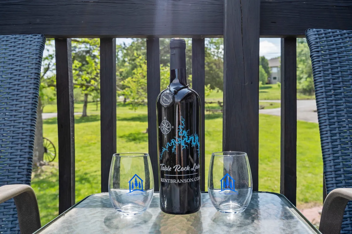 A close-up of a table set for two outdoors with a bottle of wine and glasses, elevated by a soft sunset glow in the background. The setup suggests celebration, relaxation, and shared moments, perfect for a romantic evening by the lake.