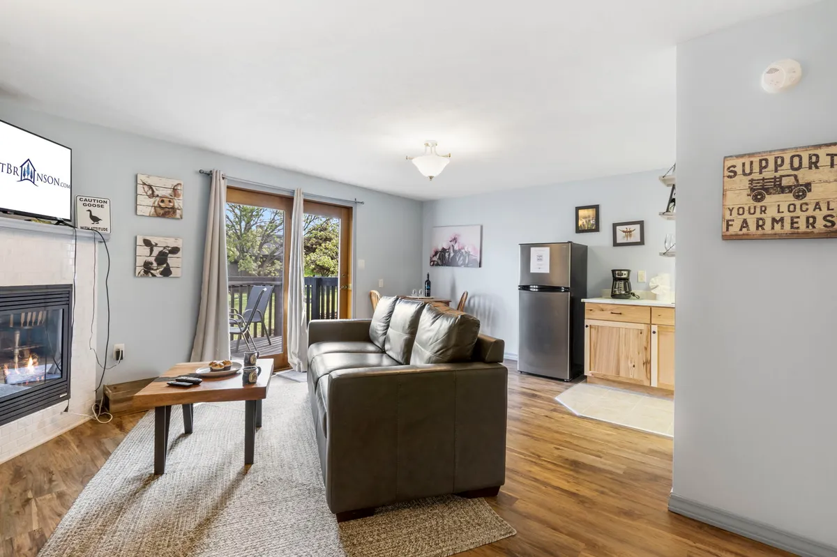 A warm, inviting space showing a kitchenette adjacent to a fireplace and balcony doors. The kitchen area is visible with essential amenities, set within a larger, cozy studio context that encourages relaxation and casual meals.