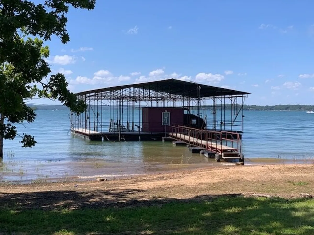 A serene lakeside dock extends over calm water, framed by trees. The area is perfect for swimming, fishing, and sunbathing, with space for guests to gather and enjoy water activities or simply relax by the shore.