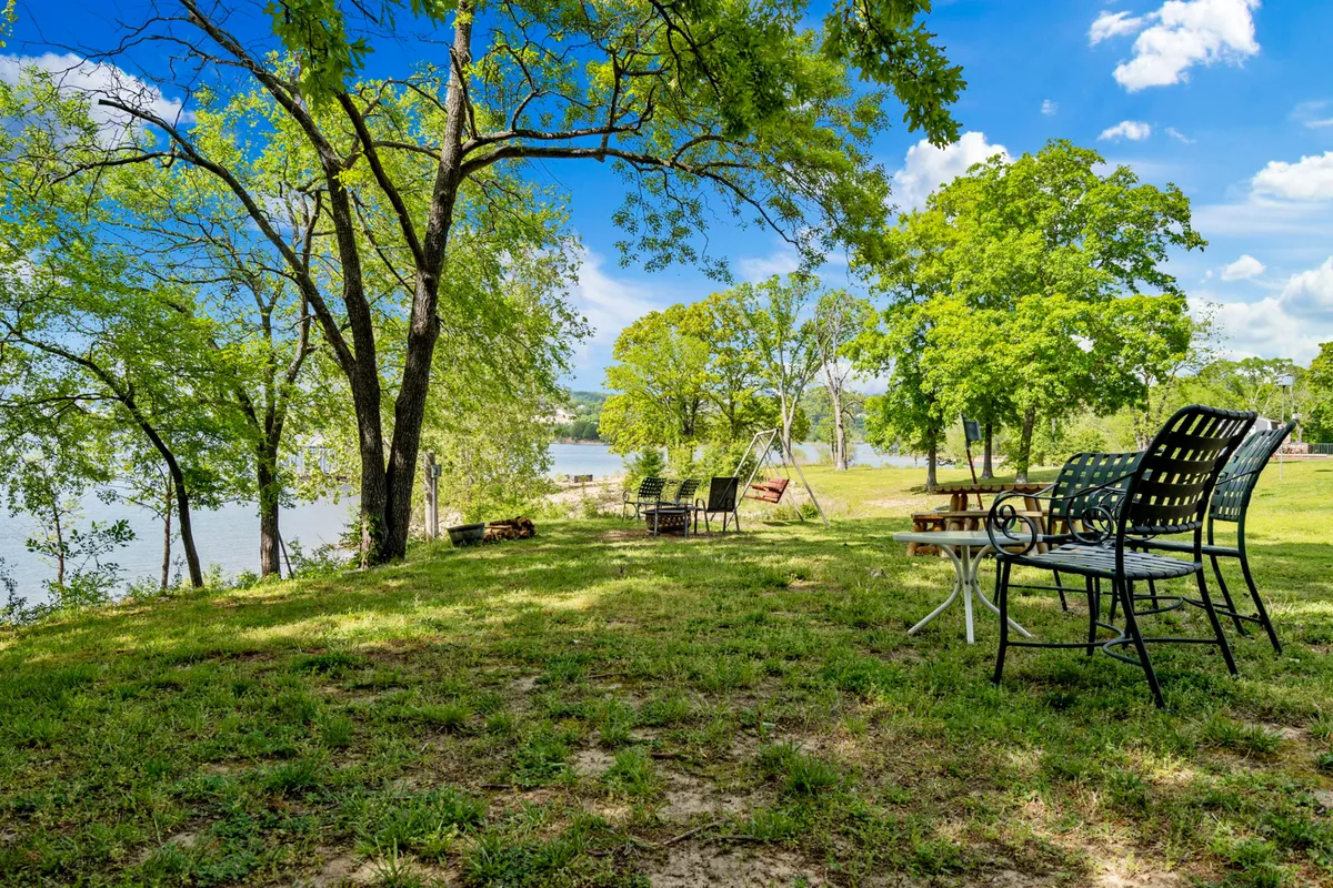 A peaceful outdoor setup with chairs and a table shaded by trees, overlooking the water. This area is perfect for picnics, casual conversations, and relaxing with friends or family, embodying the community spirit of the property.